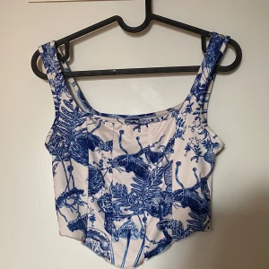 Blåvit korsett-topp  - Superfin korsett-topp från SHEIN i vitt med blått botaniskt mönster av svampar och växter. Toppen har breda axelband, croppad passform och markerad midja. Perfekt för dig som vill sticka ut med en unik och konstnärlig vibe. Frakt tillkommer