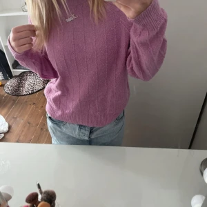 Rosa stickad tröja - Superfin Rosa stickad tröja med diskret ribbat mönster. Tröjan har rund halsringning och långa ärmar med breda muddar. Perfekt att styla med jeans för en chill och trendig look.