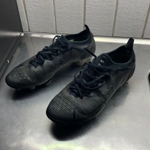 Svarta Nike fotbollsskor strl 43 - Säljer ett par svarta Nike fotbollsskor i storlek 43. Skorna har en modern, slimmad design med snörning och mönstrad ovandel i syntetmaterial. Yttersulan har fasta dobbar för bra grepp på planen. Perfekta för dig som vill ha stilrena och funktionella skor till matchen. Köpta för 3199 special design på Nikes hemsida