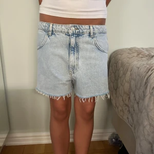 Ljusblå jeansshorts med fransig kant - Snygga ljusblå jeansshorts med klassisk femficksmodell och fransig rå kant nertill. Tillverkade i denim