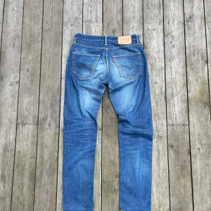 Levi's 505 blå jeans straight fit - Klassiska Levi's 505 jeans i mellanblå tvätt med snyggt slitna detaljer. Modellen har rak passform, fem fickor och ikonisk läderpatch bak i midjan. Jeansen är tillverkade i bomull och har orange sömmar samt silverfärgade nitar. Perfekta för en avslappnad och tidlös stil.