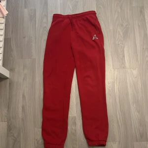 Röda Jordan mjukisbyxor med logga - Snygga röda mjukisbyxor från Jordan med klassisk Jumpman-logga på höften. Byxorna har resår och snörning i midjan samt muddar vid bensluten för en skön och sportig look. Perfekta för chill eller träning.