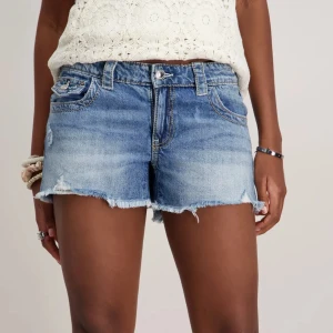 Blå jeansshorts från Gina Tricot - Snygga blå jeansshorts från Gina Tricot med råa, fransiga kanter och klassisk femficksdesign. Shortsen har bakfickor med lock och knapp, samt en ljus tvätt för en fräsch sommarkänsla. Perfekta för varma dagar och enkel att matcha med allt.