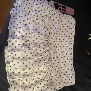 Vit volangkjol med svarta prickar - Supersöt kort volangkjol i vitt med svarta prickar. Kjolen har flera lager volanger som ger en fluffig och lekfull look. Perfekt för dig som gillar en trendig och feminin stil. Resår i midjan för skön passform.