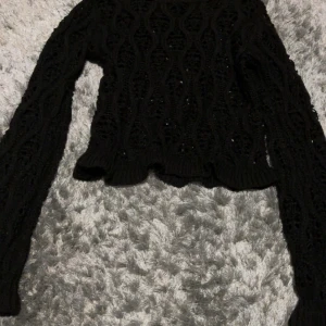 Svart stickad tröja från Divided (hm) - Svart stickad tröja från Divided i storlek XXS. Tröjan har ett vågigt, hålmönstrat stickat mönster och är croppad med långa ärmar. Perfekt för lager-på-lager och snygg till både jeans och kjol.