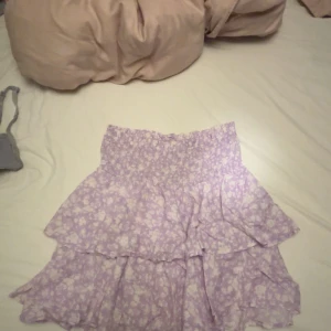 Ljuslila blommig volangkjol Samsa - Supersöt kort volangkjol från Samsa Collection i ljuslila med vitt blommönster. Kjolen har smock i midjan för skön passform och dubbla volanger som ger en flowy och lekfull look. Perfekt för varma dagar när du vill känna dig extra söt. Behövs strykas. 