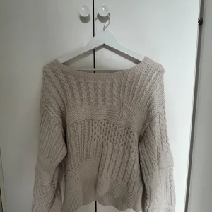 Beige stickad tröja med knyt i ryggen - Säljer en beige stickad tröja med olika kabelstickade mönster och snygg v-ringning i ryggen med knytband. Tröjan har lång ärm och en lite loose passform, perfekt för lager på lager under höst och vinter.💕💕