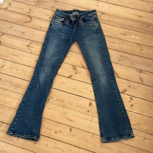 Blå bootcut jeans från LTB W25 L32 - Snygga blå jeans från LTB med klassisk bootcut-modell och låg midja. Jeansen har fem fickor, slitna detaljer vid benslut och är tillverkade i ett mjukt jeansmaterial. Perfekta för dig som gillar en retro vibe och vill ha ett par jeans som sticker ut lite extra.