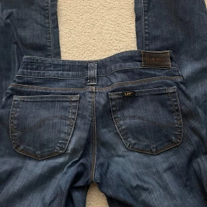 Blå jeans från Lee - Säljer ett par klassiska blå jeans från Lee med snygga kontrastsömmar och bakfickor med vågig detalj.