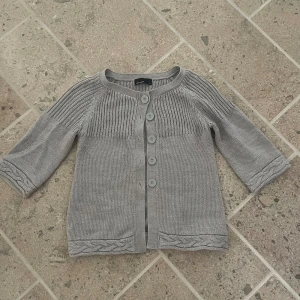 Grå kofta med trekvartsärmar - Snygg grå stickad kofta från Vero Moda med trekvartsärm och knappar framtill. Lite ribbade stickningar. Står storlek M men passar S, inga synliga defekter!💗
