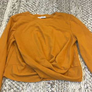 Senapsgul långärmad tröja från Zara - Säljer en senapsgul långärmad tröja från Zara. Tröjan har en enkel rund halsringning och en snygg twistad detalj framtill. Storlek S.