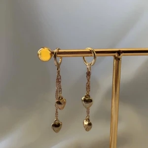 Guldiga örhängen med hjärtan - Snygga guldiga örhängen med dubbla kedjor och små hjärtan som hänger längst ner. Perfekta för dig som vill ha en söt men ändå trendig detalj till din look. Hjärtformade hängen ger en romantisk vibe och kedjorna ger extra rörelse.