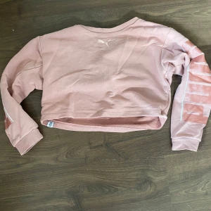 Rosa croppad tröja  - Säljer en ljusrosa croppad tröja från Puma med tryckt logga på bröstet och stort tryck längs ena ärmen. Tröjan har långa ärmar och är gjord i mjuk bomullsmix. Perfekt för en chill och sportig look. Tröjan har några flöckar som syns på bilderna men det är inget man tänker på, tröjan är i barnstorlek men mins inte vilken storlek men kan kolla om så önskas🌸