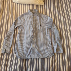 Blårandig skjorta Polo Ralph Lauren - Snygg blårandig skjorta från Polo Ralph Lauren med klassisk krage och broderad logga på bröstet. Skjortan har lång ärm, knappar framtill och är i ett mjukt bomullstyg. Passar riktigt bra till sommaren och hösten, perfekt för dig som gillar stilrena och tidlösa plagg! Hör gärna av dig vid intresse om fler bilder eller frågor😊