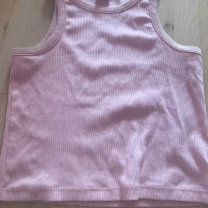 Rosa ribbad linnetopp från Lindex - Säljer en ljusrosa ribbad linnetopp från Lindex. Toppen är ärmlös med klassisk rund halsringning och har en tight passform. Perfekt för varma dagar eller som lager under en skjorta. Materialet är mjukt och stretchigt för extra komfort.