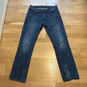 Blå jeans från East West W31 L32 - Snygga blå jeans från East West med klassisk femficksdesign och raka ben. Jeansen är tillverkade i 100% bomull och har en cool tvättad look med lätt slitning på låren. Perfekta för en avslappnad och stilren outfit.