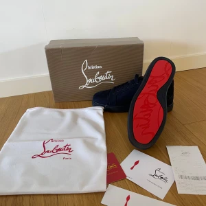 Christian Louboutin skor - Säljer ett par mörkblå sneakers från Christian Louboutin med klassisk röd sula och snörning. Skorna har en stilren design i mocka och diskreta detaljer. Perfekta för dig som vill sticka ut med exklusiva skor.