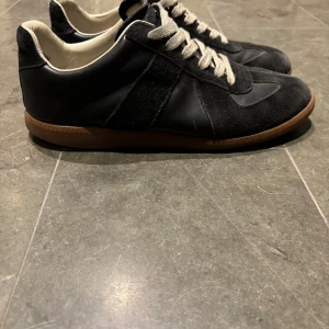 Svarta sneakers i mocka och skinn - Maison Margiela GAT-sneakers, herr EU 41 (passar 42) Använda – normal slitage på sulan och lite fläckningar på mockan. Skinnen är helt oskadat. Lite sliten look på gummisulan. De passar dig med storlek 42 tack vare passformen.  Sulan är ganska sliten. Små bruksspår i mocka