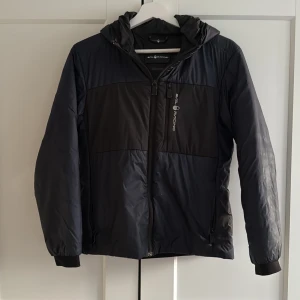Sail Racing Jacka (Svart/Mörkblå) - Säljer en svart pufferjacka från Sail Racing som är perfekt till hösten och blåsiga dagar då den är windproof, den är i bra skick men det finns täcken av användning. Priset går att diskuteras vid snabb affär!