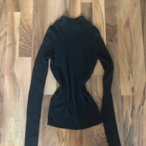 Svart polotröja  - Slimmad svart polotröja med lång ärm, perfekt för lager-på-lager. Gjord i mjuk ull som håller dig varm under kyliga dagar. Enkel och stilren design som funkar till allt. Polokragen ger en clean look och tröjan sitter tajt mot kroppen. 