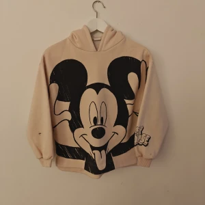 Disney hoodie - Supermysig beige hoodie från Zara x Disney med stor svartvit Mickey Mouse-tryck framtill. Tröjan har huva, långa ärmar och ribbade muddar. Perfekt för dig som älskar Disney och vill ha en chill och cool stil.