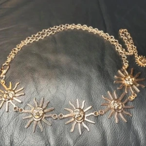 Kedjebälte i guld med solberlocker – perfekt för boho, witchy & festival looks - Lyft din outfit med detta kedjebälte i guldtonad metall, dekorerat med uttrycksfulla solhängen. Perfekt för dig som gillar bohemisk, alternativ eller Y2K-inspirerad stil. Justerbar längd med hake gör det enkelt att anpassa. Avslutas med en liten dekorativ sol som detalj.  • Längd: ca 110 cm • Solhängen: ca 5 cm höga • Material: Metall • Skick: Helt nytt, oanvänt  Styla över klänning, byxor eller midjekort topp för en lager-på-lager-look. Ett statement som passar både vardag, festival och fest.  