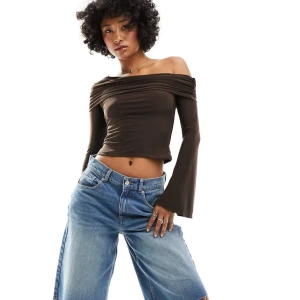 Brun offshoulder croppad topp - Snygg brun offshoulder topp med croppad passform och långa utsvängda ärmar. Tunn och stretchig, perfekt för att skapa en cool och trendig look. Sitter tight över axlarna och har en draperad effekt upptill.