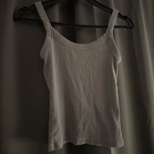 Grå ribbad linnetopp - En enkel och stilren grå ribbad linnetopp med breda axelband. Perfekt att matcha med jeans eller kjol för en avslappnad look. Mjuk och stretchig känsla som sitter skönt på kroppen.