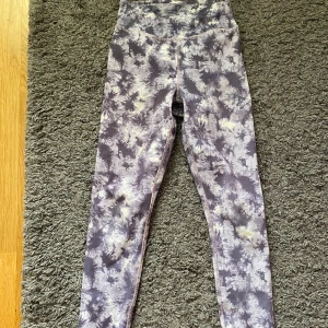 Lila tie-dye leggings med hög midja - Snygga leggings med lila och vitt tie-dye mönster och hög midja. Perfekta för träning eller chill, med stretchigt material som sitter skönt. Mönstret ger en cool vibe och de är lätta att matcha med en oversized hoodie eller crop top. Har ett litet hål på knät. Pris kan diskuteras 