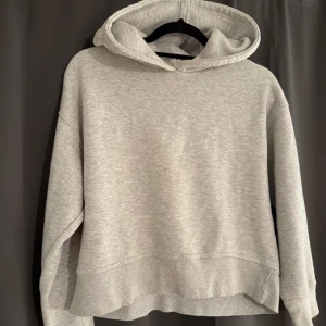 Ljusgrå hoodie med huva - Enkel och stilren ljusgrå hoodie med huva och långa ärmar. Tröjan har en relaxed passform och är tillverkad i mjuk bomullsblandning, perfekt för chill dagar eller när du vill ha en clean look.