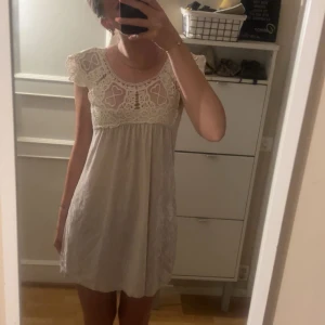 Söt kort vit klänning med spets - Supersöt kort klänning i ljusbeige/vit med vackert virkad spets upptill och fjärilsärmar. Klänningen har en luftig passform och i sammet material , perfekt för varma dagar. 
