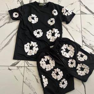 Svart t-shirt från Denim Tears med tryck - Svart t-shirt från Denim Tears med unika vita grafiska tryck över hela tröjan. Klassisk rund hals och korta ärmar. Skön passform och tillverkad i mjuk bomull, perfekt för dig som gillar streetwear med edge.