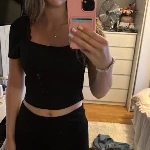 Svart ribbad croppad topp H&M S - Svart croppad topp från H&M med ribbad struktur och korta ärmar. Toppen har en fyrkantig ringning och sitter snyggt figurnära. Perfekt att matcha med höga jeans eller kjol för en clean look.