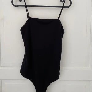 Svart bodysuit - En stilren svart bodysuit från BikBok i storlek XS men passar även S. Modellen har smala axelband och ärmlös design, perfekt att styla med jeans eller kjol. Mjuk och stretchig bomullsblandning som sitter snyggt på kroppen. Använd enstaka gång