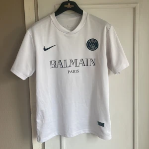 Vit PSG x Balmain fotbollströja Nike - Snygg vit PSG fotbollströja i samarbete med Balmain och Nike. Tröjan är i dri fit vilket innebär att det är träningsmaterial. Men tröjan används ofta som en vardaglig T-shirt men även också träning. Storlek S men passar även mindre M.