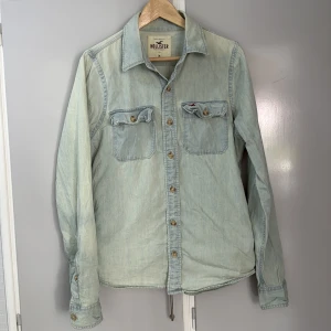 Ljusblå jeansskjorta från Hollister medium - Snygg ljusblå jeansskjorta från Hollister med klassisk krage, två bröstfickor med lock och knappar framtill. Skjortan har långa ärmar och är tillverkad i 100% bomull. 