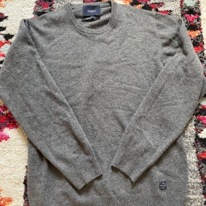 Grå stickad tröja från Signal - En klassisk grå stickad tröja från Signal, tillverkad i Italien. Tröjan har rund halsringning, långa ärmar och en liten patch nertill. Perfekt för lager-på-lager och enkel att matcha med jeans eller chinos.