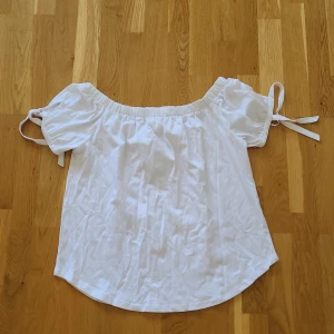 Vit offshoulder topp från H&M - Superfin vit offshoulder topp från H&M med korta ärmarn och snörning på ärmarna. Har en avslappnad passform som ger en luftig känsla. Helt ny, nypris 99 kr. 