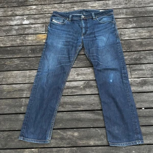 Diesel Thanaz blå jeans W36 L34 - Säljer ett par klassiska blå Diesel Thanaz jeans med snygg tvätt och raka ben. Jeansen har fem fickor, diskreta slitningar och stretch för extra komfort. Perfekta för dig som gillar en tidlös denimlook med coola detaljer.