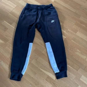 Svarta Nike mjukisbyxor med vita detaljer - Svarta mjukisbyxor från Nike i storlek S med vita paneler längs underbenen. Byxorna har resår i midjan, muddar vid bensluten och klassisk Nike-logga på låret. Perfekta för chill eller träning, riktigt sköna och stilrena. Rätt stor i storlek så passar folk med storlek M också.