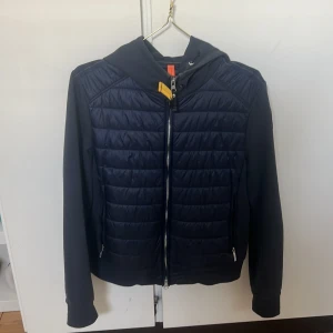 Mörkblå pufferjacka från Parajumpers - Snygg mörkblå pufferjacka från Parajumpers med huva och dragkedja. Jackan har quiltad framsida och rygg, samt mjuka ärmar.Perfekt för dig som vill ha en stilren och sportig look. Inga defekter! Den passar i alla storlekar jag är en xs-s person men jackan är i L då det var den ända som fanns i lager på Nk i den modellen. Kom privat för mer bilder på! Kom med pris förslag! 