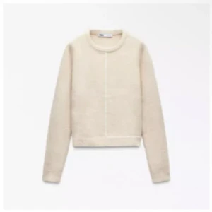 Beige stickad tröja från Zara - En stilren beige stickad tröja från Zara med rund halsringning och långa ärmar. Tröjan har en rak passform och en diskret söm framtill som ger en modern touch. Perfekt att matcha med jeans eller kjol för en clean look. Den sitter som xs