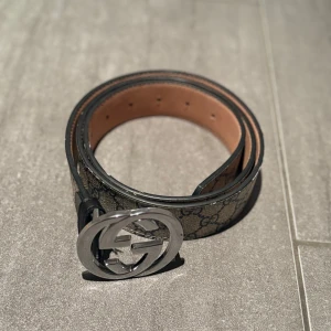 Gucci GG Supreme bälte med silverdetalj -  Äkta Gucci GG Supreme bälte med klassiskt monogrammönster i beige och grått. Snyggt rundat spänne i silverfärgad metall med GG-logga. Bältet är gjort i skinn. Se bild (5) för att de är en liten defekt där pga användning o de gör att priset sänks. Köpt för 4899kr i Italien på Gucci för ca 3-4 år sedan men mitt pris 949kr. Hör av dig vid minsta fundering👍😁
