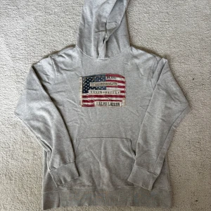 Ralph lauren denim&supply flag hoodie - Snygg grå hoodie från Ralph Lauren Denim & Supply med stor amerikansk flagga i patchwork-stil på bröstet. Tröjan har huva, magficka och är tillverkad i 100% bomull. Väldigt populär tröja! Inga defekter!