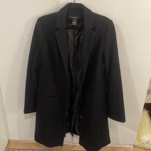 Svart kappa från Sara Kelly Ellos - Stilren svart kappa från Sara Kelly för Ellos. Klassisk design med krage, knappar framtill och två fickor. Långärmad och helfodrad som går ner till knäna på mig som är 170cm. Passar till många outfits och är enkel att matcha. Hör av dig vid funderingar!❣️