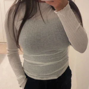 Vit blus - Säljer en vit långärmad tröja med tight passform. Tröjan har en enkel och stilren look med rund halsringning och tunna, diskreta ränder i materialet. Perfekt att styla med jeans eller kjol för en clean vibe. Aldrig använd. Kan passa en xs/s då den är stretchig