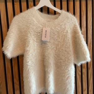 Fluffig vit stickad tröja från Wera - Supermjuk och fluffig vit stickad tröja från Wera med korta ärmar och rund hals. Tröjan har en cool, lurvig textur som ger en trendig look och passar perfekt när du vill sticka ut lite extra. Enkel att styla med både jeans och kjol. Tveka inte på att höra av er vid frågor eller intresse!