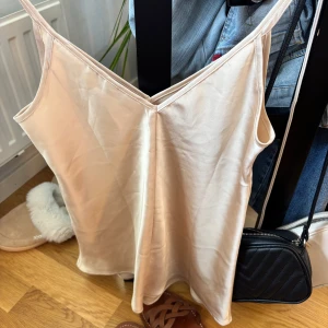 Champagnefärgad linnetopp i satin - Snygg champagnefärgad linnetopp i satin med smala axelband och v-ringning. Toppen kan båda va festlig eller ett sov plagg!