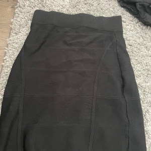 Svart tight kjol med ribbad midja - Säljer en svart tight kjol med bred ribbad midja och diskreta sömdetaljer. Kjolen har en enkel och stilren design som sitter snyggt på kroppen. Perfekt för dig som gillar minimalistisk stil och vill ha en kjol som är lätt att matcha.