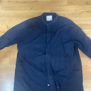 Mörkblå henley-skjorta i bomull XL - Stilren mörkblå henley-skjorta i bomull med ståkrage och knappar framtill. Skjortan har lång ärm och en clean look utan synliga fickor eller mönster. Perfekt för dig som gillar enkel och modern stil.